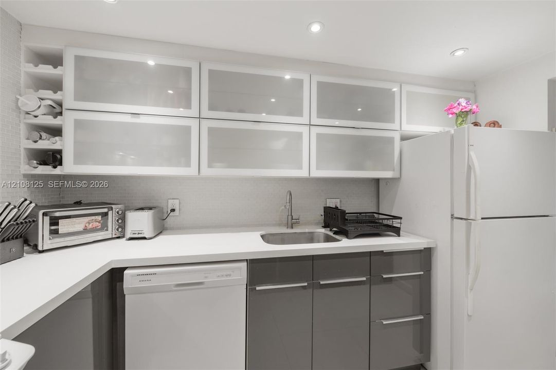 Kitchen featuring high-gloss charcoal base cabinetry, upper cabinets with frosted glass inserts, solid-surface countertops, recessed ceiling lighting, and integrated wine storage