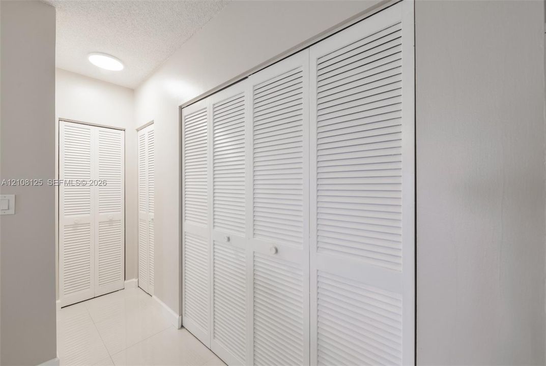 White louvered closet doors, neutral wall finish, and tile flooring