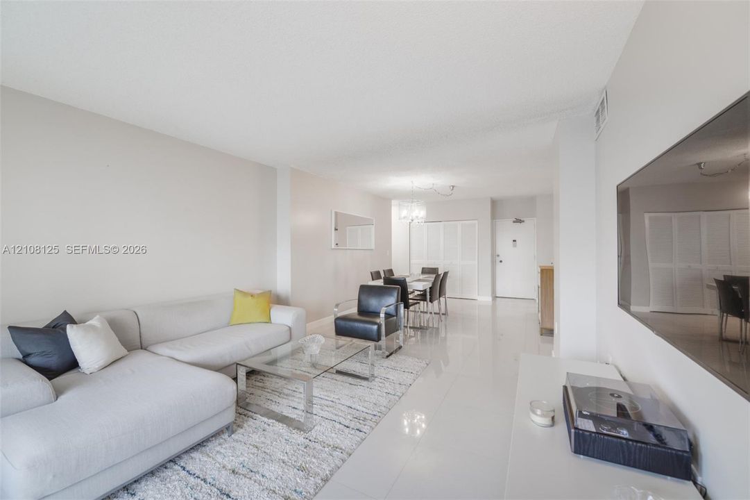 Open-concept interior featuring light-toned tile flooring, neutral wall paint, a multi-light chandelier, and full-height bi-fold closet doors