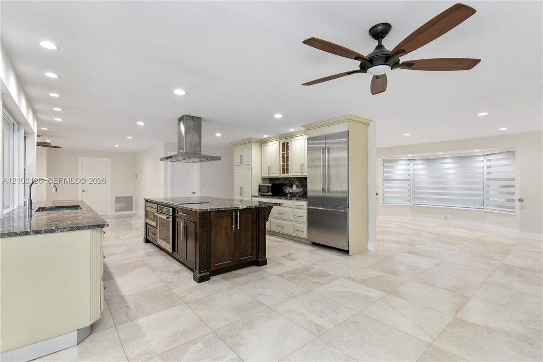 Kitchen featuring a center island with dark wood-finish cabinetry, stainless steel appliances, a stainless steel range hood, stone countertops, and tile flooring