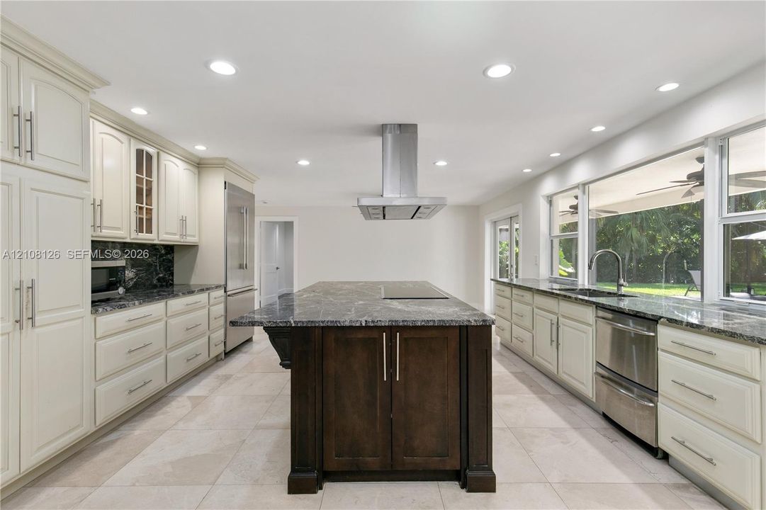 Kitchen featuring light-toned cabinetry, a dark-toned center island with a built-in cooktop, stainless steel range hood, stone-finish countertops, and tile flooring
