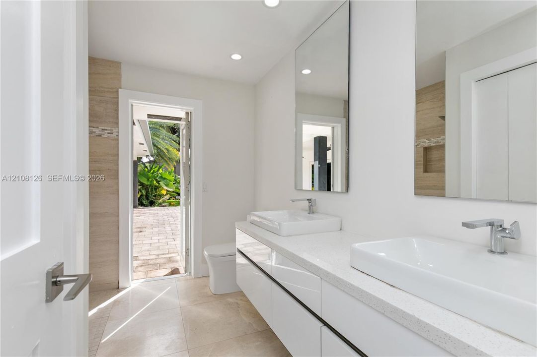 Modern floating vanity with dual rectangular vessel sinks, quartz countertops, and polished chrome faucets, complemented by wall-to-wall mirrors and stone tile flooring