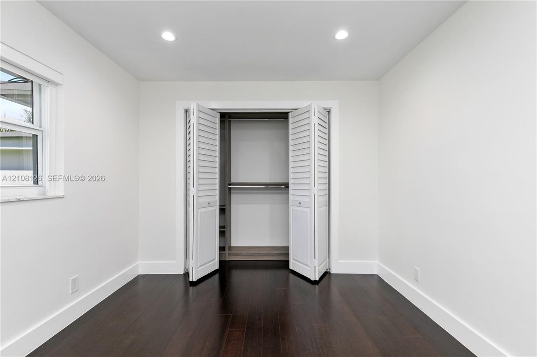 Neutral interior featuring dark wood-finish flooring, recessed lighting, and a closet with white louvered bi-fold doors and built-in shelving