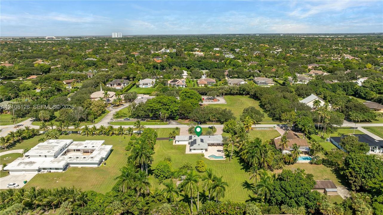 Aerial perspective featuring an expansive lot, established tropical landscaping, mature canopy trees, and an integrated swimming pool
