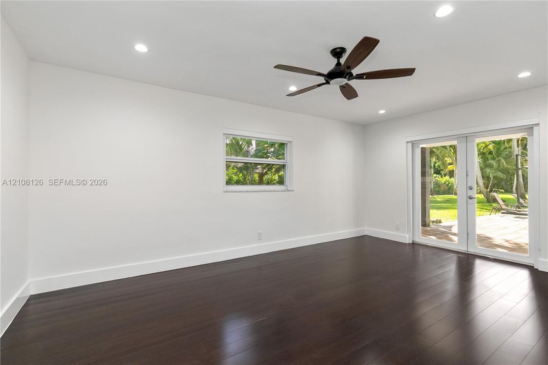 Dark wood-finish flooring, recessed lighting, ceiling fan, single-hung window, and glass-paned double doors