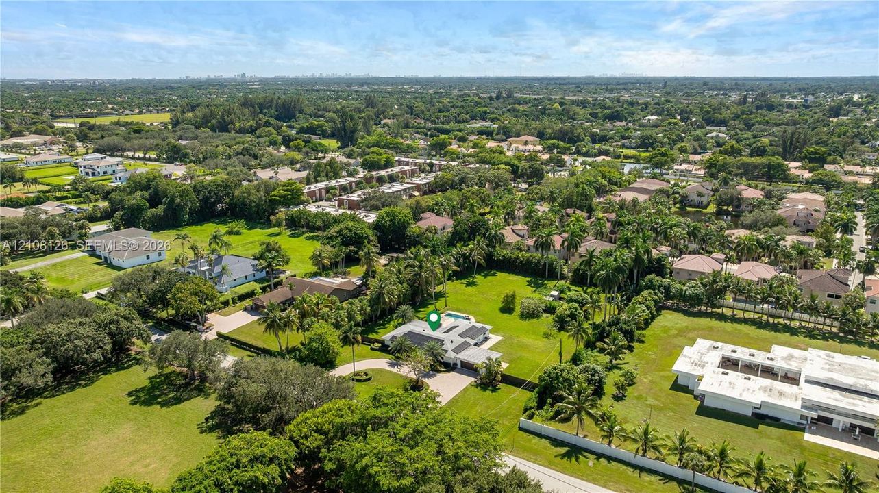 Aerial perspective of a sprawling property featuring a circular driveway, expansive manicured grounds, mature palm trees, and an in-ground swimming pool