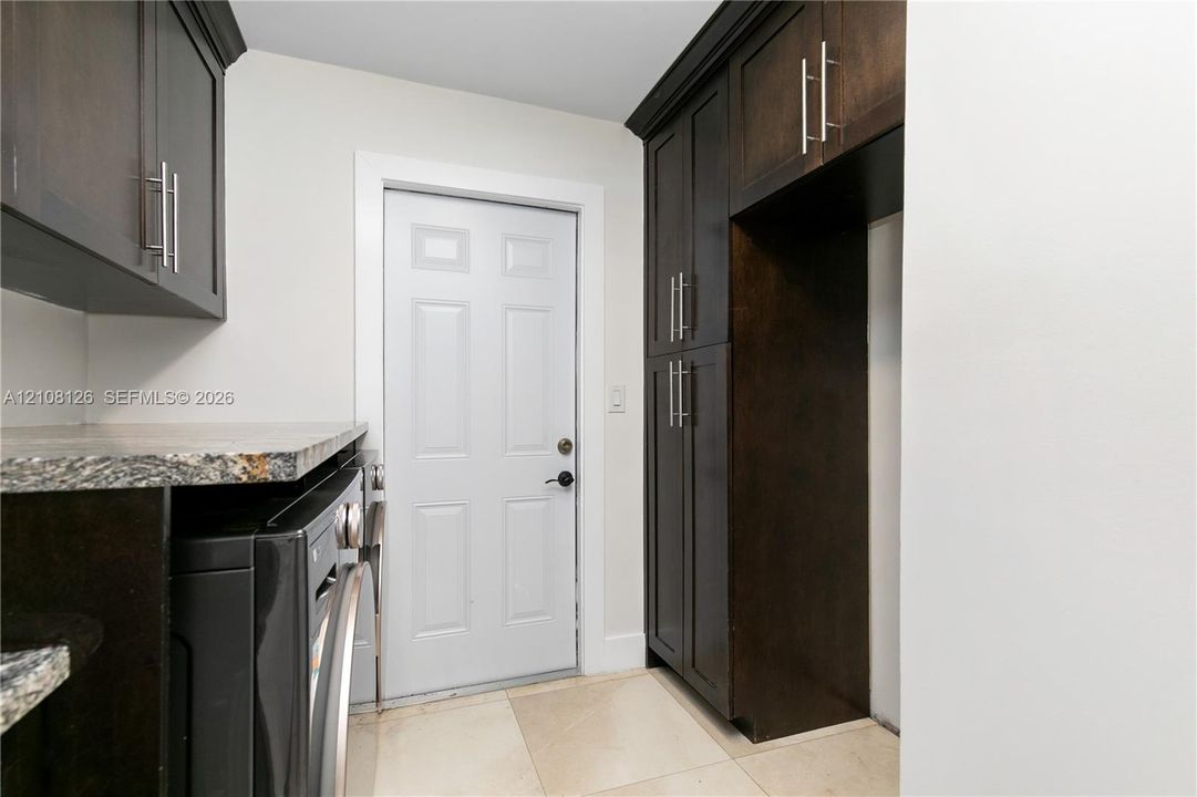 Dark-toned cabinetry featuring stainless steel hardware, stone-finish countertops, tile flooring, and a paneled exterior door