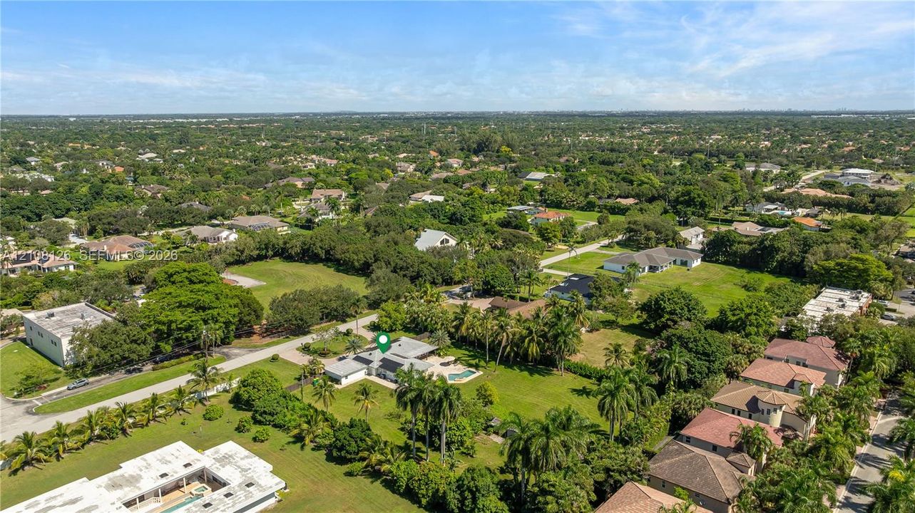 Aerial perspective featuring a sprawling lot with an inground pool, expansive lawn, mature palms, and paved driveway access
