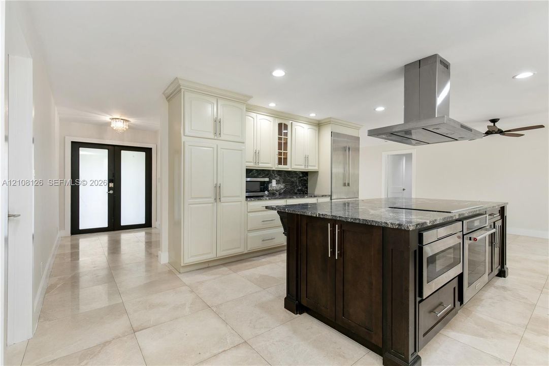 Kitchen featuring an expansive center island with stone countertop, stainless steel professional-grade appliances, built-in cabinetry, polished stone flooring, and a stainless steel ceiling-mounted vent hood