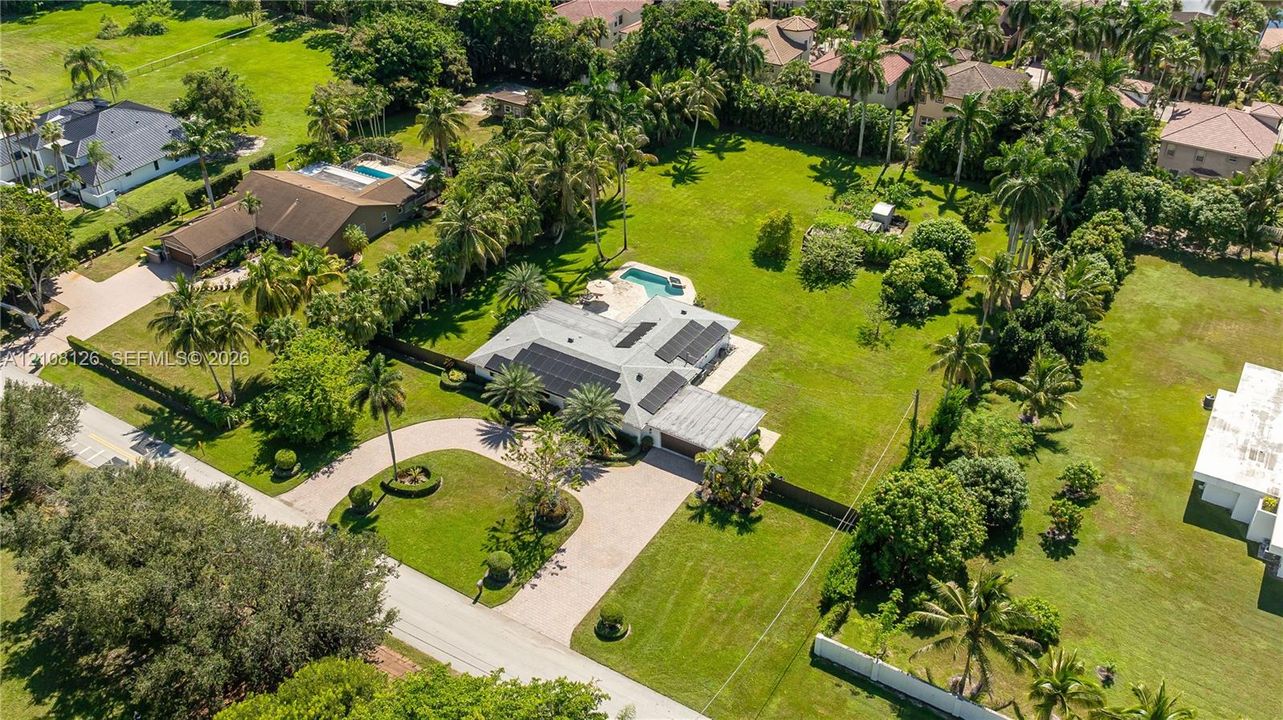 Aerial perspective of an expansive lot featuring a multi-gabled residence, a paved circular driveway, a private in-ground swimming pool, and solar panel arrays