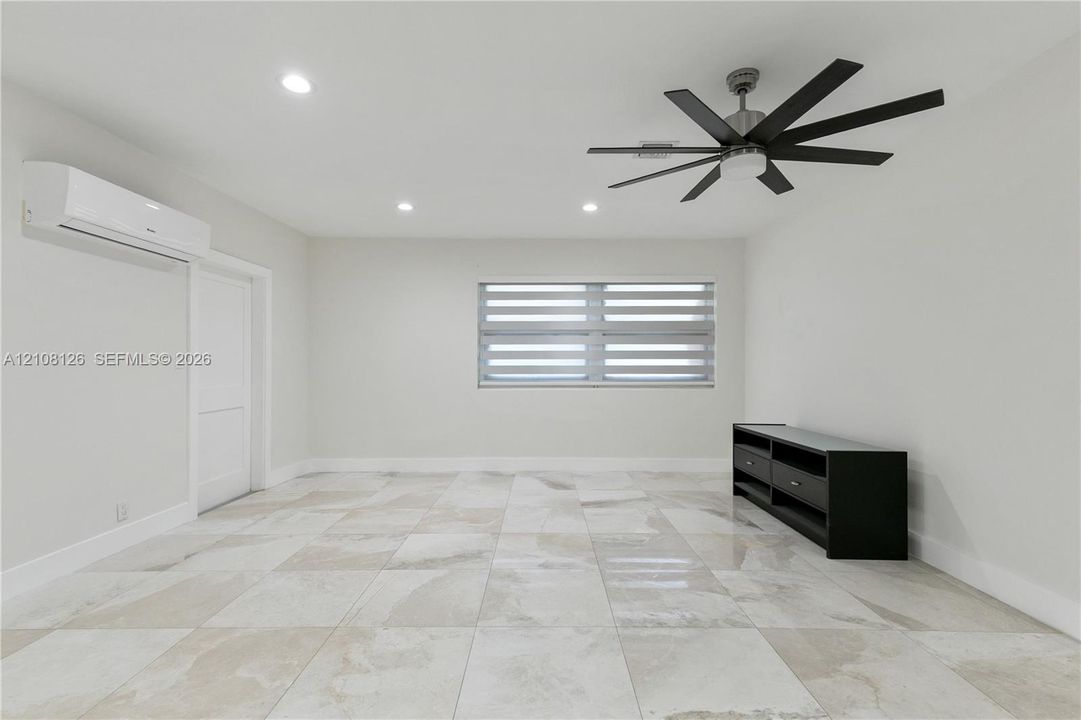 Interior space featuring large-format stone-finish floor tiling, recessed lighting, a multi-blade ceiling fan, a wall-mounted ductless climate control unit, and window blinds