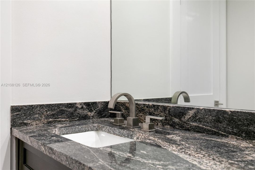 Stone countertop with integrated backsplash, under-mount basin, and metallic widespread faucet, complemented by a wall-mounted mirror