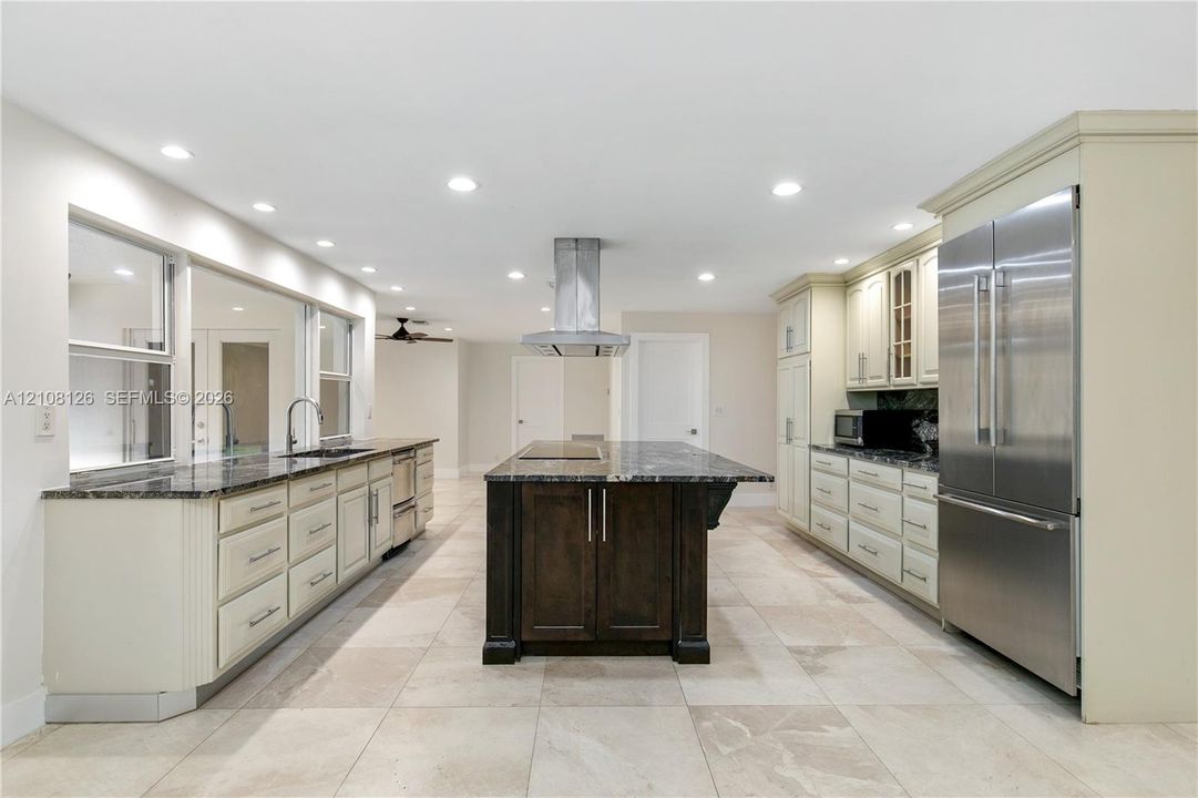 Kitchen featuring a central island with a stone countertop, custom cabinetry, stainless steel refrigerator, stone-tiled flooring, and recessed ceiling lighting