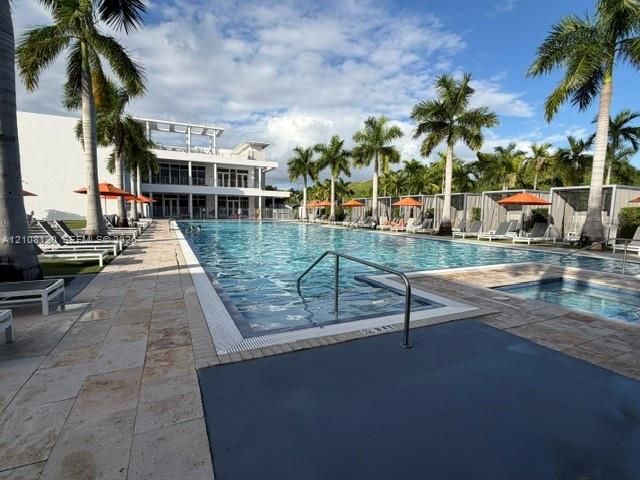 Large swimming pool with stone-tiled decking, attached spa, and metal-framed cabanas surrounded by mature palm trees