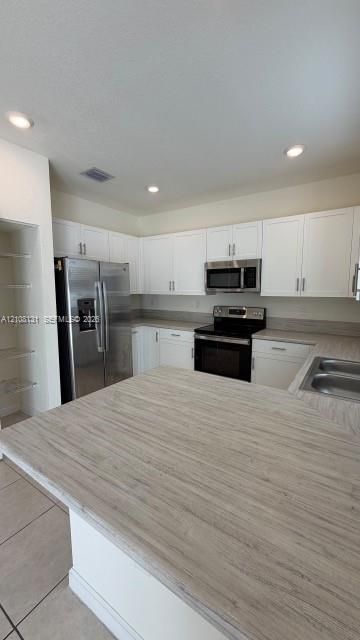 Kitchen featuring white shaker-style cabinetry, stainless steel appliances, wood-finish laminate countertops, built-in pantry shelving, and recessed lighting