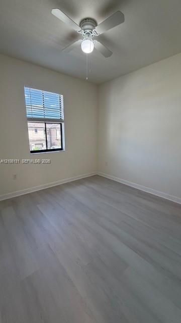 Neutral-toned interior space featuring wood-finish flooring, a ceiling fan with integrated lighting, and a single-pane window with horizontal blinds