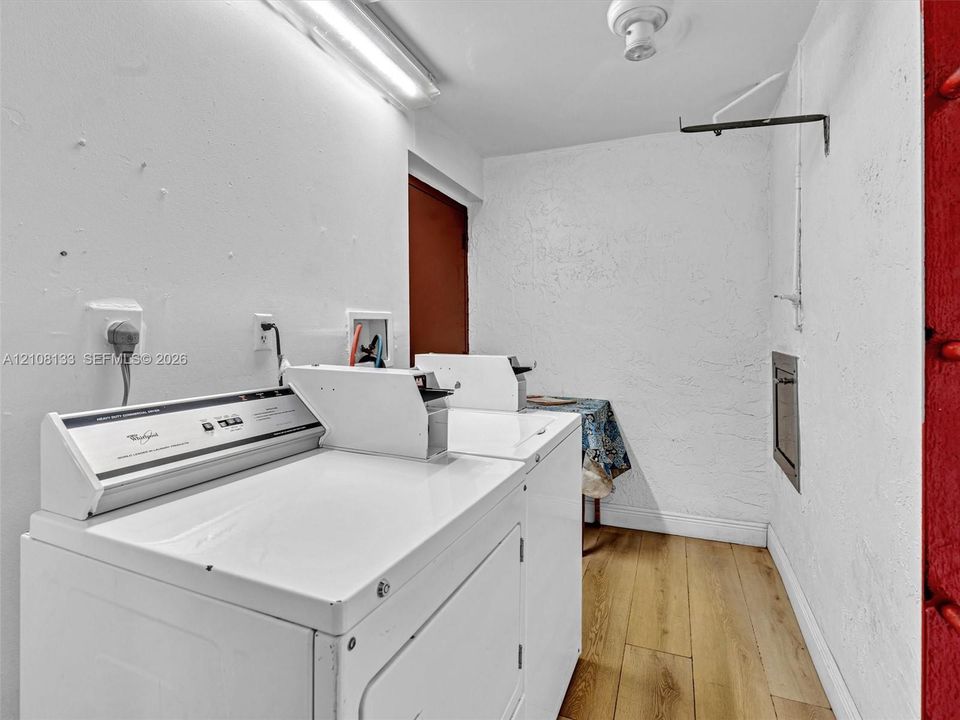 Laundry area featuring wood-finish flooring, fluorescent overhead lighting, and built-in laundry supply connections
