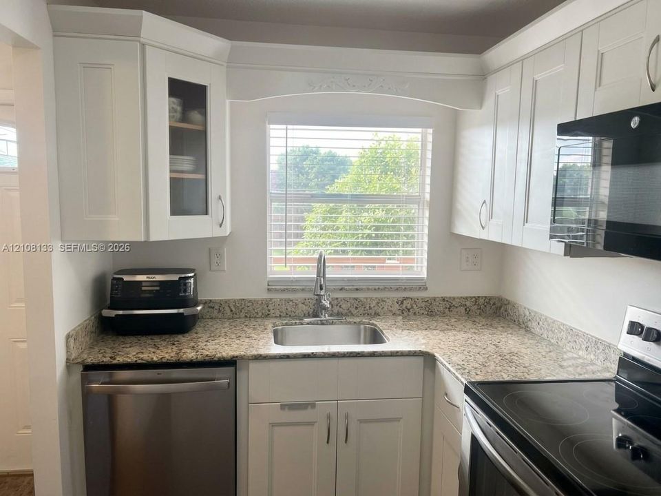 Kitchen featuring white shaker-style cabinetry with glass-front accents, stone countertops, stainless steel sink with gooseneck faucet, and stainless steel dishwasher
