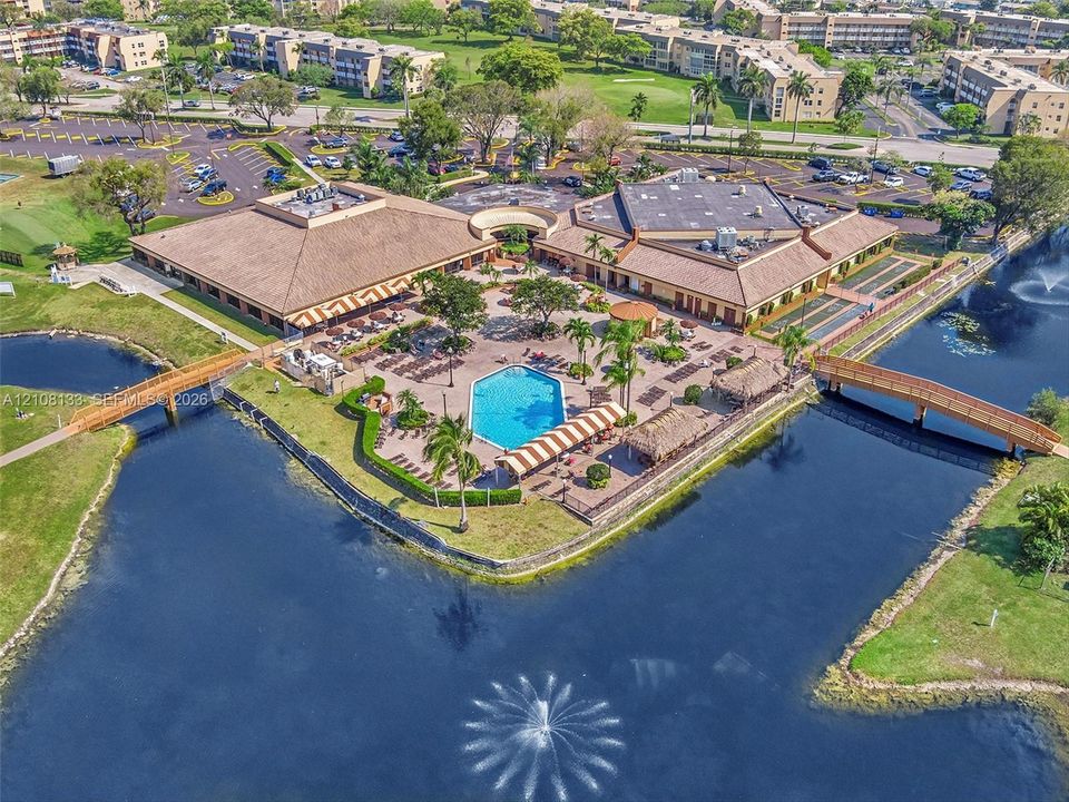 Exterior aerial featuring a central swimming pool, paved patio, perimeter water feature with a fountain, and two wooden pedestrian bridges