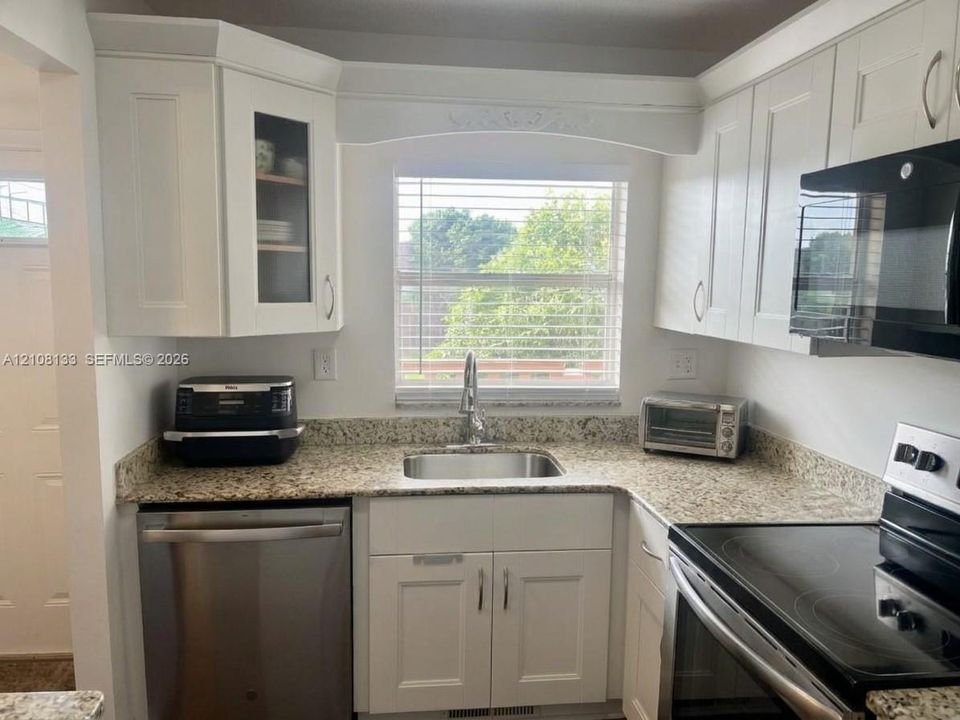 Kitchen featuring white cabinetry with glass-panel detailing, stone-patterned countertops, stainless steel undermount sink, and integrated stainless steel appliances