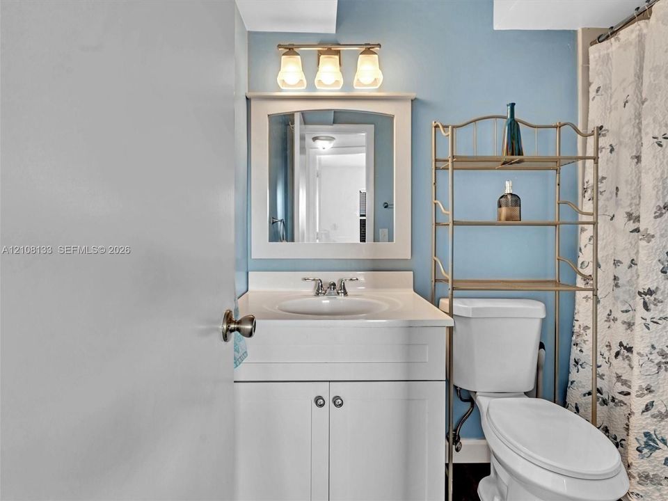 Bathroom featuring a white vanity with integrated basin, polished metal faucet, three-light fixture, and wall-mounted mirror