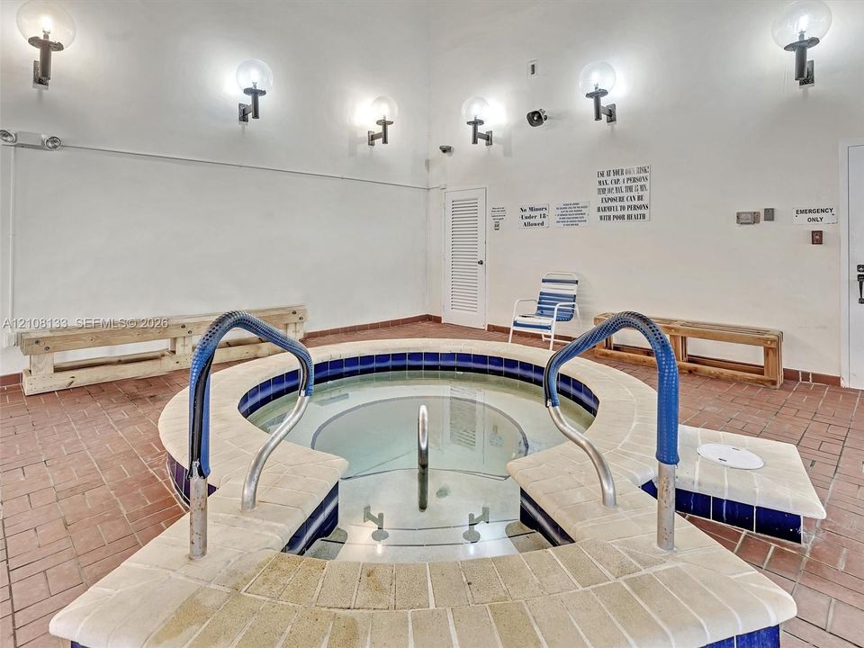 Indoor spa featuring a tiled circular basin, built-in bench seating, globe wall sconces, and brick flooring