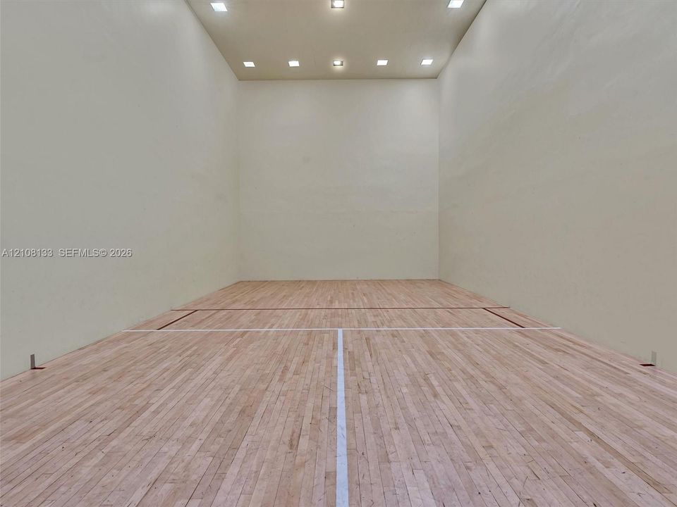 Recreation room featuring wood-finish flooring, high-contrast court markings, solid-surface wall paneling, and recessed ceiling lighting