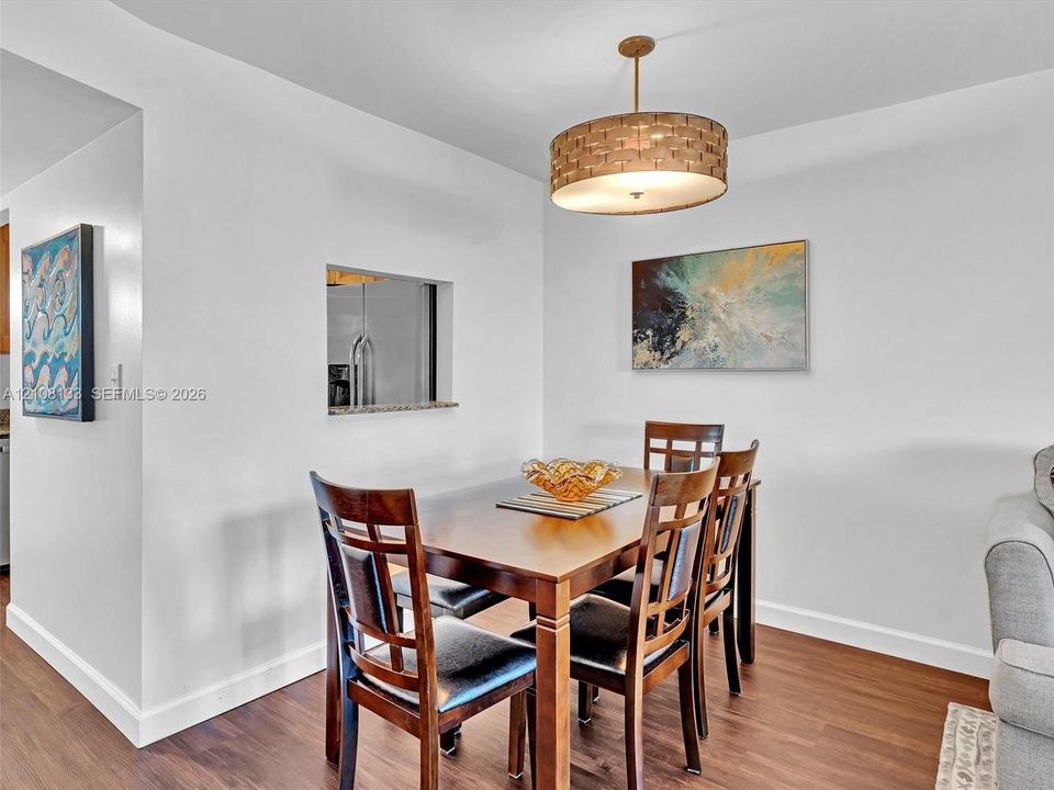 Dining area featuring wood-finish flooring, a contemporary drum pendant light fixture, and a pass-through wall opening with a stone-surface ledge