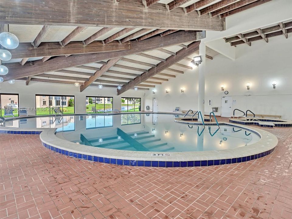 Indoor swimming pool featuring an expansive design, exposed wood-beam ceiling, tile surround, and brick flooring