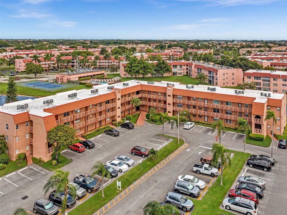 Multi-story residential complex featuring stucco exterior, flat roofing, designated surface parking, and manicured landscaping with mature palm trees