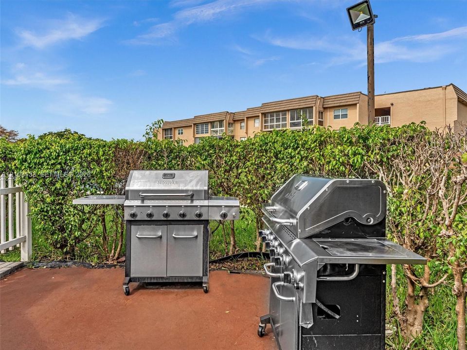 Outdoor grilling area featuring two stainless steel gas grills, a concrete patio surface, and privacy hedges
