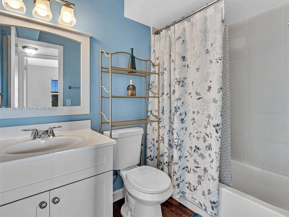Bathroom featuring a white vanity cabinet with an integrated basin, a three-light vanity fixture, a framed mirror, and a tile-surround bathtub