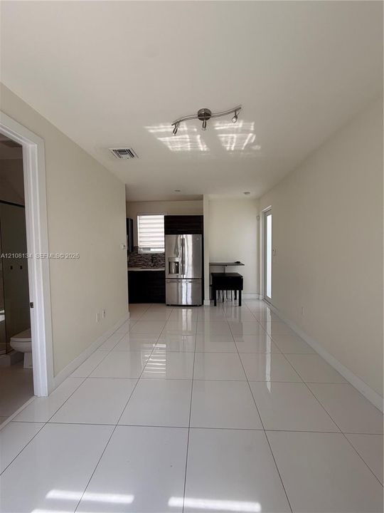 Open-concept interior featuring polished large-format tile flooring, stainless steel refrigerator, dark cabinetry, and adjustable multi-light ceiling fixture