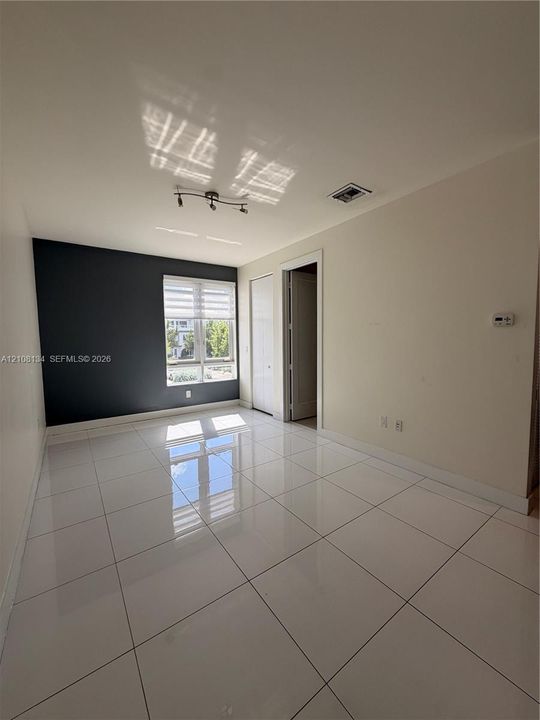 Polished white tile flooring, charcoal accent wall, multi-pane window with zebra-style shade, and adjustable track lighting fixture