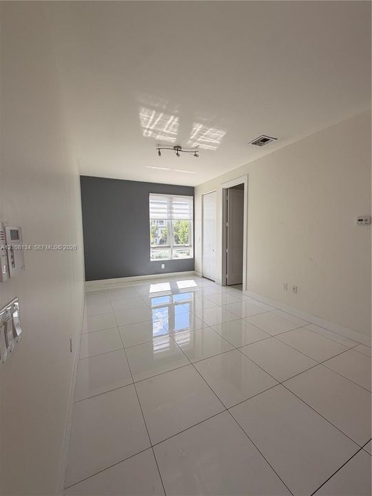 Interior space featuring large-format tile flooring, a charcoal accent wall, multi-pane window with blinds, and ceiling-mounted track lighting