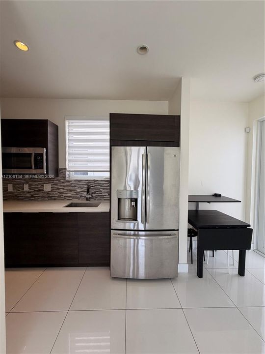 Kitchen featuring dark wood-finish cabinetry, stainless steel refrigerator with an external ice dispenser, mosaic tile backsplash, solid-surface countertops, and large-format tile flooring