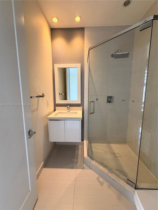 Floating white vanity with a single basin, frameless corner shower enclosure, tiled wall surround, and recessed ceiling lighting