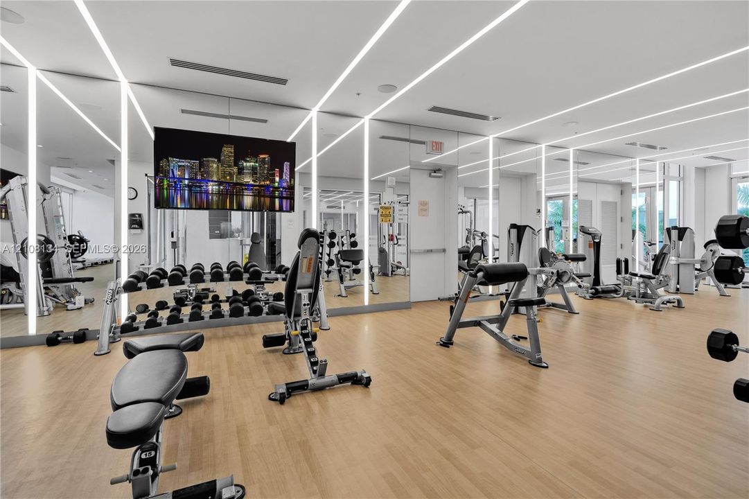 Fitness center featuring wood-finish flooring, floor-to-ceiling mirrored walls, and recessed vertical linear lighting