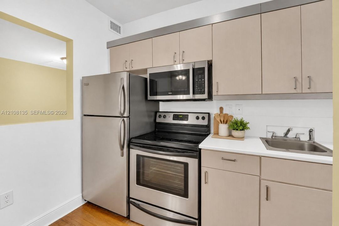 Kitchen featuring flat-panel cabinetry, stainless steel appliances, white countertops, a drop-in sink, and wood-finish flooring