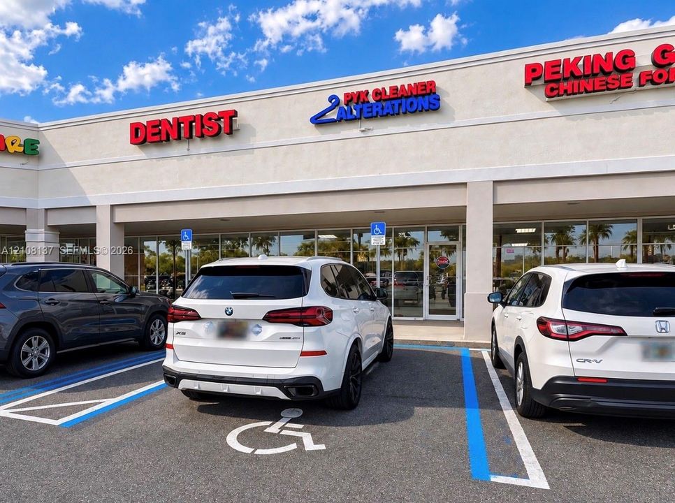 Commercial storefront featuring a stucco facade, covered walkway, large glass display windows, and designated parking spaces