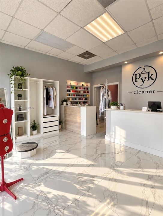 Commercial space featuring large-format tile flooring, built-in display shelving, recessed wall shelving with integrated lighting, a custom service counter, and a drop ceiling with recessed lighting