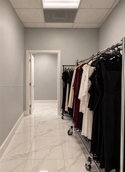 Neutral-toned interior space featuring polished tile flooring with marble-style veining, a drop-ceiling grid system, and a classic-panel swinging door