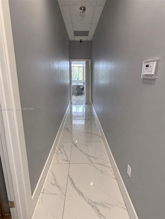 Hallway featuring large-format stone-patterned tile flooring, smooth grey-painted walls, and a recessed ceiling fixture