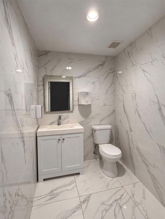 Restroom finished with floor-to-ceiling large-format stone-patterned tile, vanity featuring an integrated sink, and recessed lighting