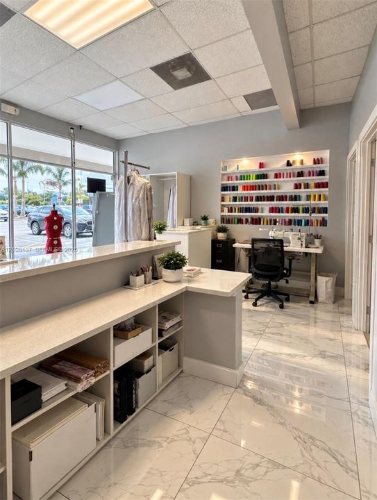 L-shaped reception counter with quartz countertop and built-in lower shelving, recessed wall shelving, and large-format tile flooring