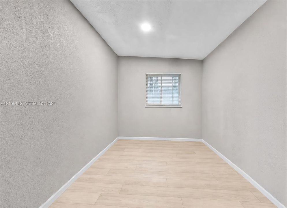 Neutral-toned interior space featuring wood-finish flooring, recessed lighting, and a window with integrated blinds