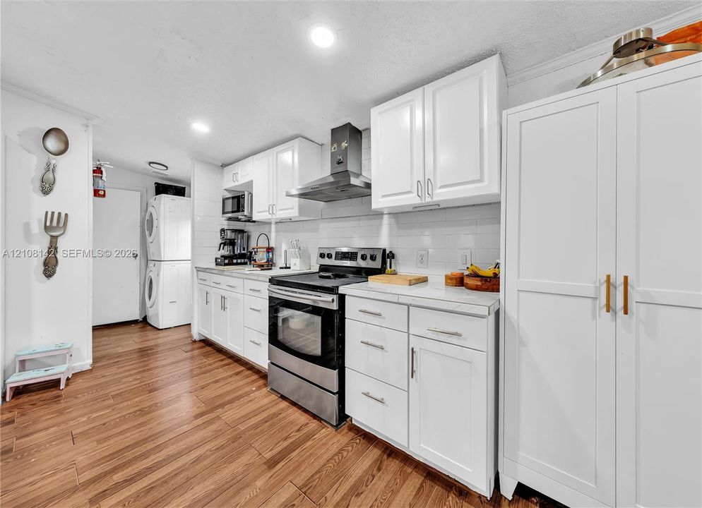 Kitchen featuring white cabinetry, stainless steel range with overhead hood, subway tile backsplash, wood-finish flooring, and built-in floor-to-ceiling storage