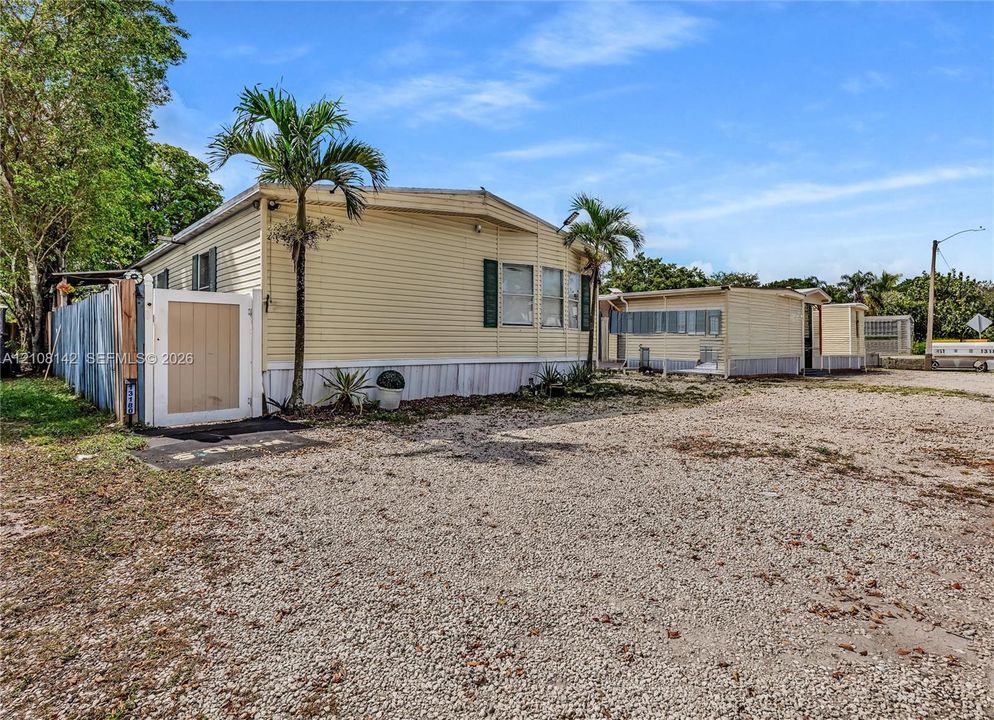 Exterior featuring light-colored horizontal siding, dual palm trees, and an attached privacy gate