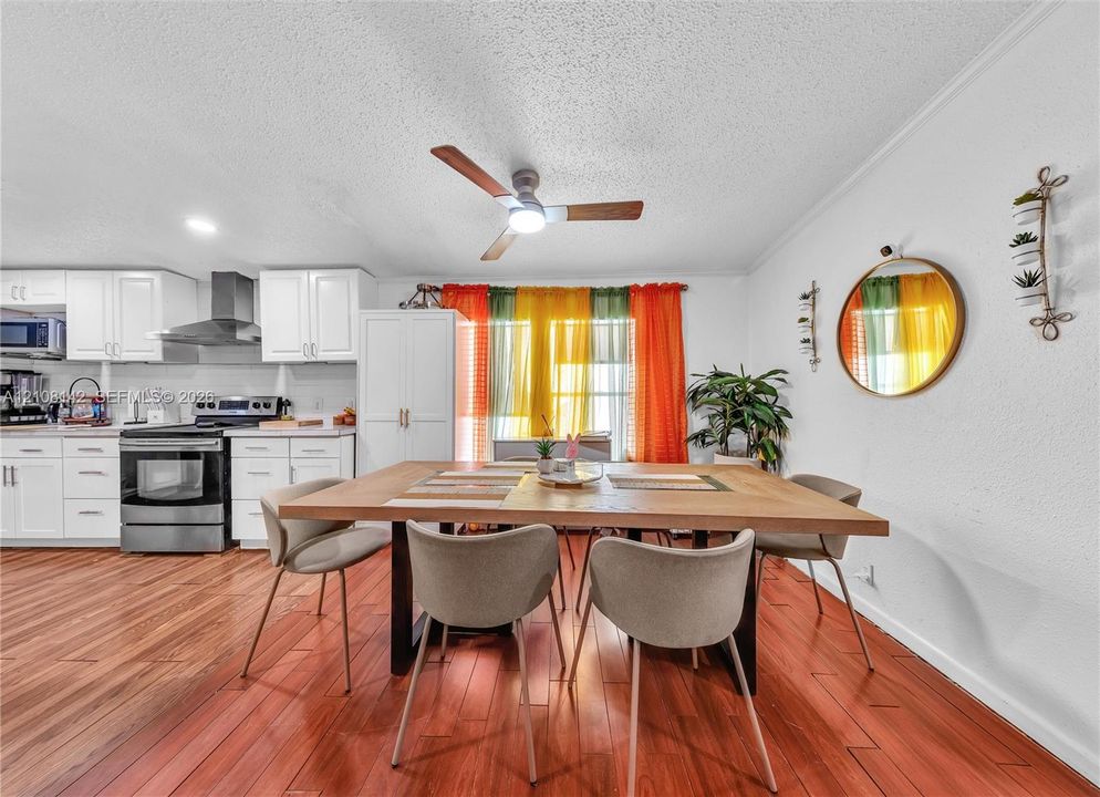Kitchen featuring white cabinetry, stainless steel range with a ventilation hood, wood-finish flooring, and a ceiling fan with integrated lighting