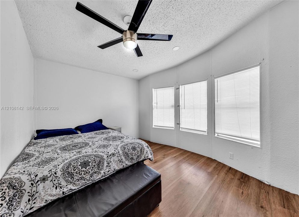 Wood-finish flooring, three large windows, and a matte black ceiling fan with integrated lighting